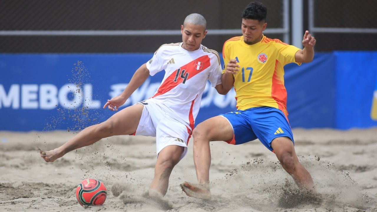 Dos jugadores de fútbol playa en una disputa intensa por el balón sobre la arena. A la izquierda, un jugador de la Selección de Perú con uniforme blanco y franja roja (número 14); a la derecha, un jugador de la Selección de Colombia con la clásica camiset