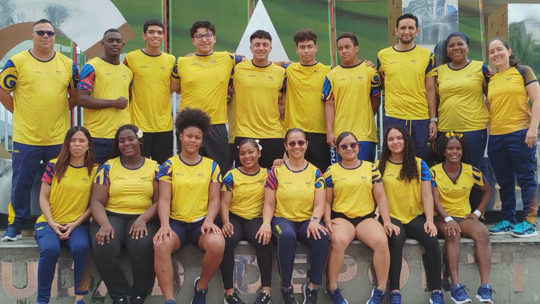 La Selección Colombia de pesas posa en grupo tras su participación en Panamá. Los deportistas visten camisetas amarillas con detalles azules y rojos, sentados y de pie en una estructura de concreto al aire libre.